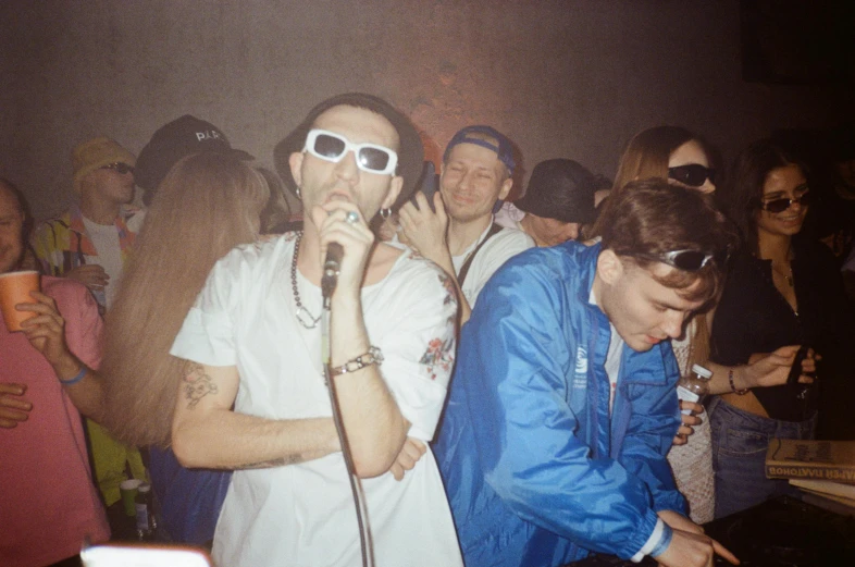 several people standing in the background and wearing sunglasses are all singing