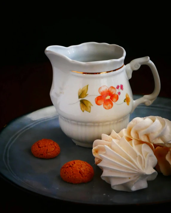 a ceramic creamer filled with icing next to cookies