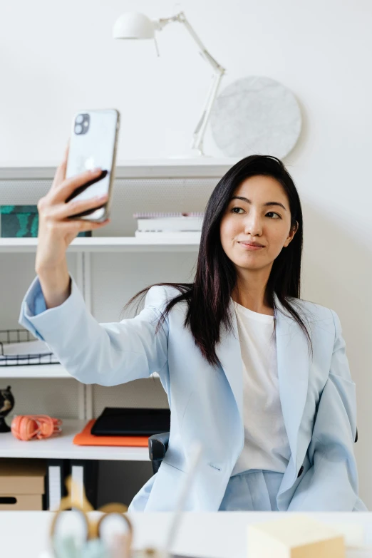 a woman sitting in a chair taking a selfie with her cellphone