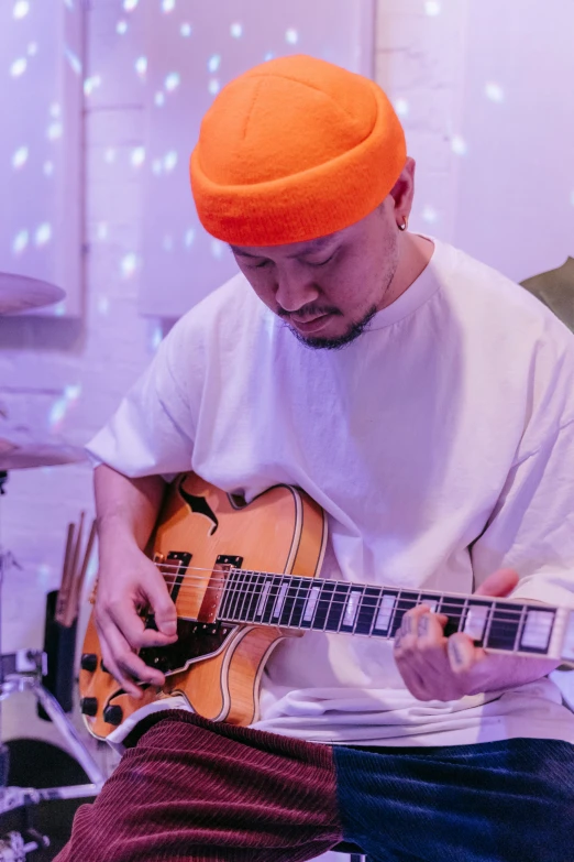 a man with an orange cap plays his guitar