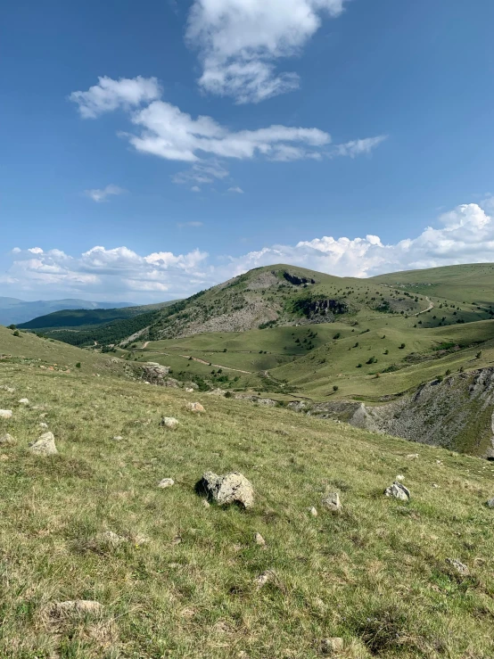 a grassy hillside with rocky slopes beneath blue skies