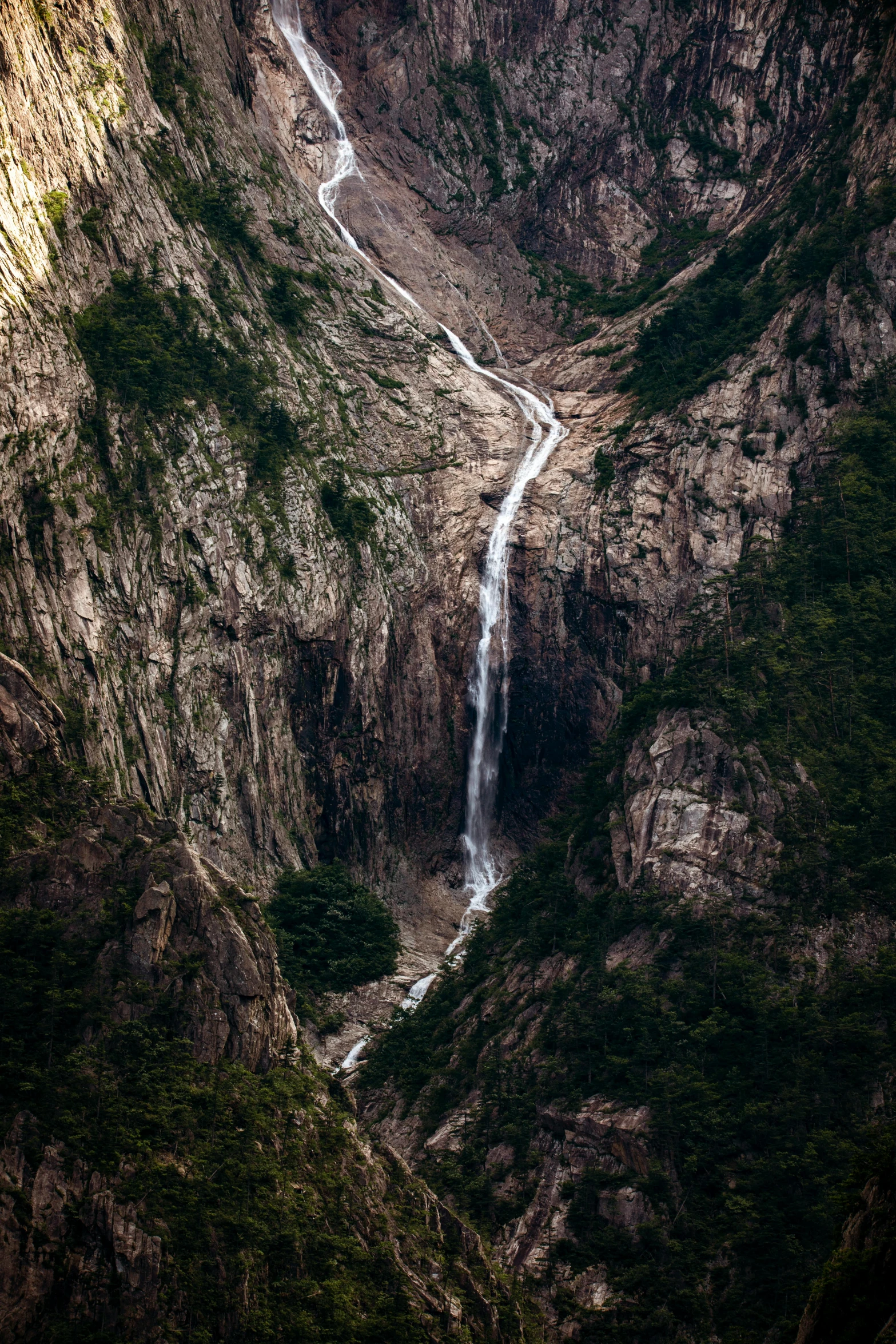 a waterfall is in between two mountains and there are trees on the side