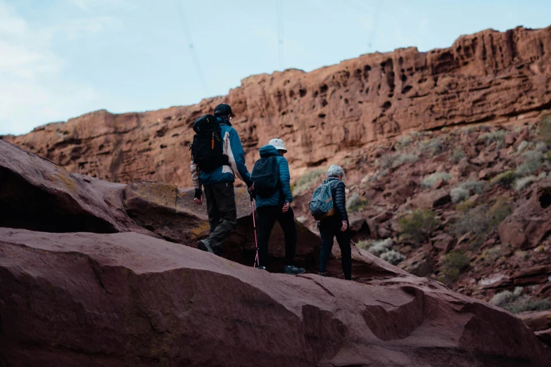 three people hiking up a mountain to reach a ledge