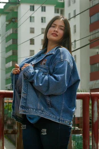 a woman wearing a denim jacket standing by a fence