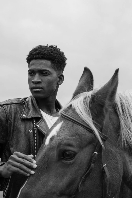 young man wearing a jean jacket, standing next to a horse
