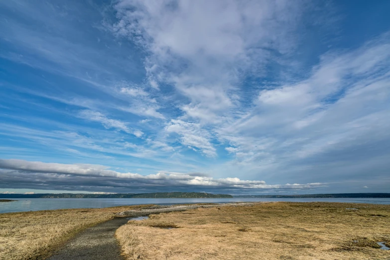 a blue cloudy sky, some clouds, and an inlet next to a beach