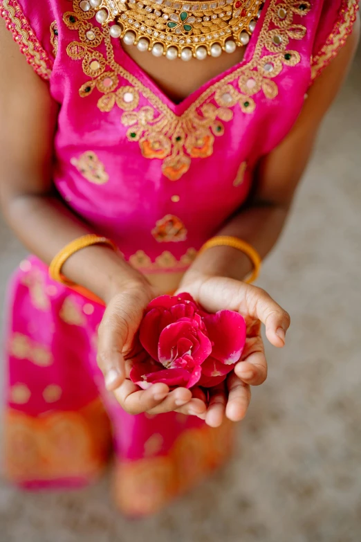 a small girl wearing gold jewelry holding a pink rose