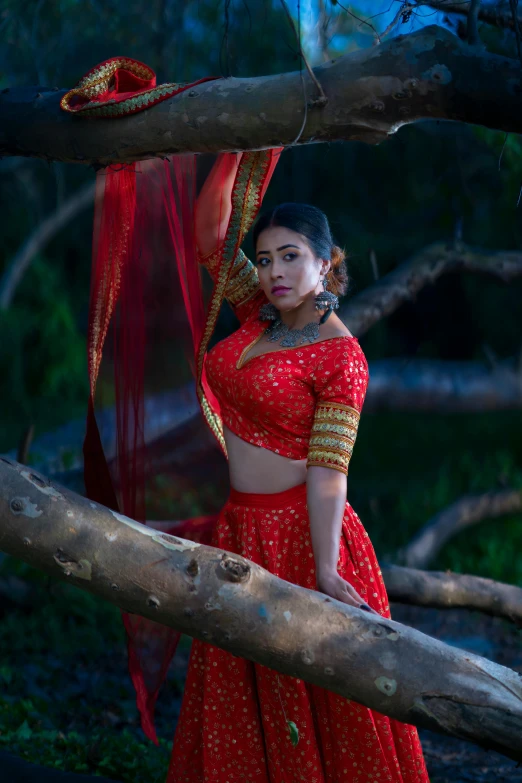 a woman wearing a red dress poses by a tree