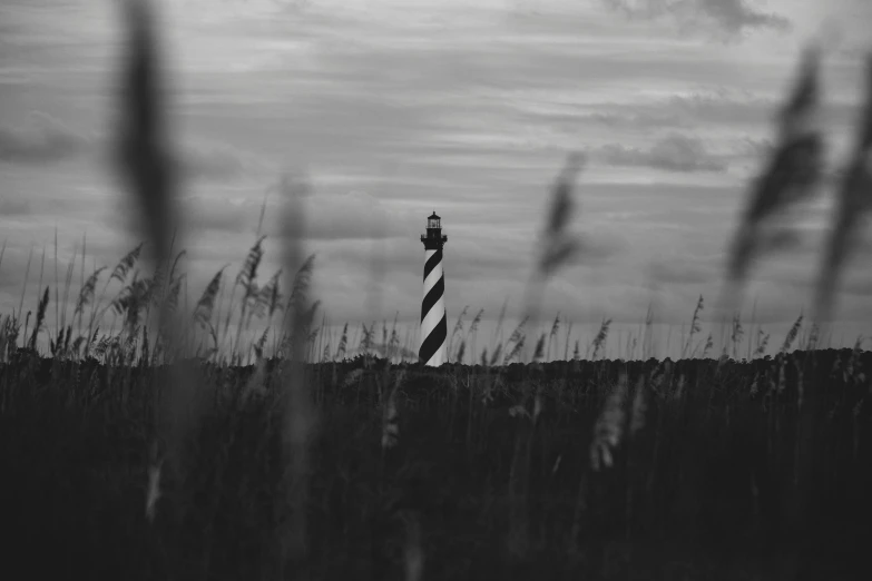 a tall lighthouse tower near some grass under a cloudy sky