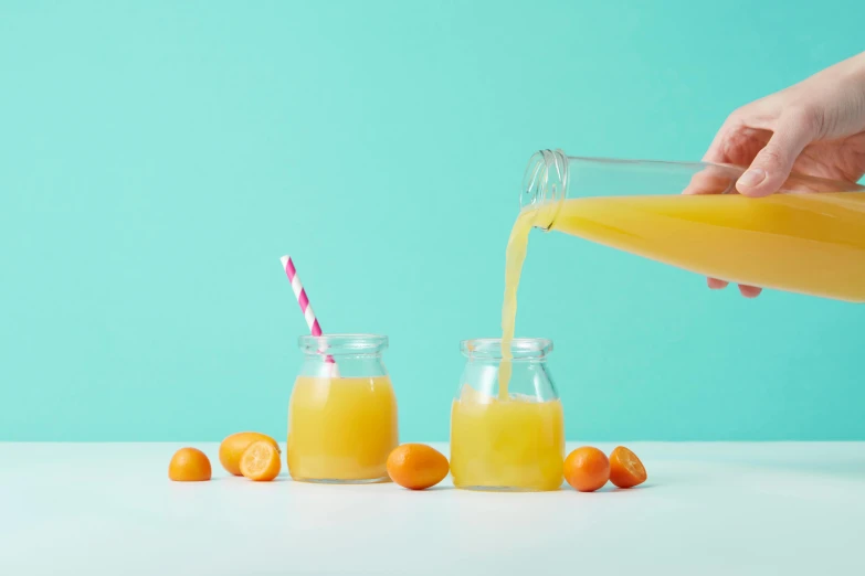 the hand is pouring orange juice into two small jars