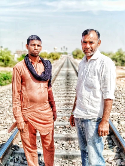 two men standing on railroad tracks with one of them facing the camera