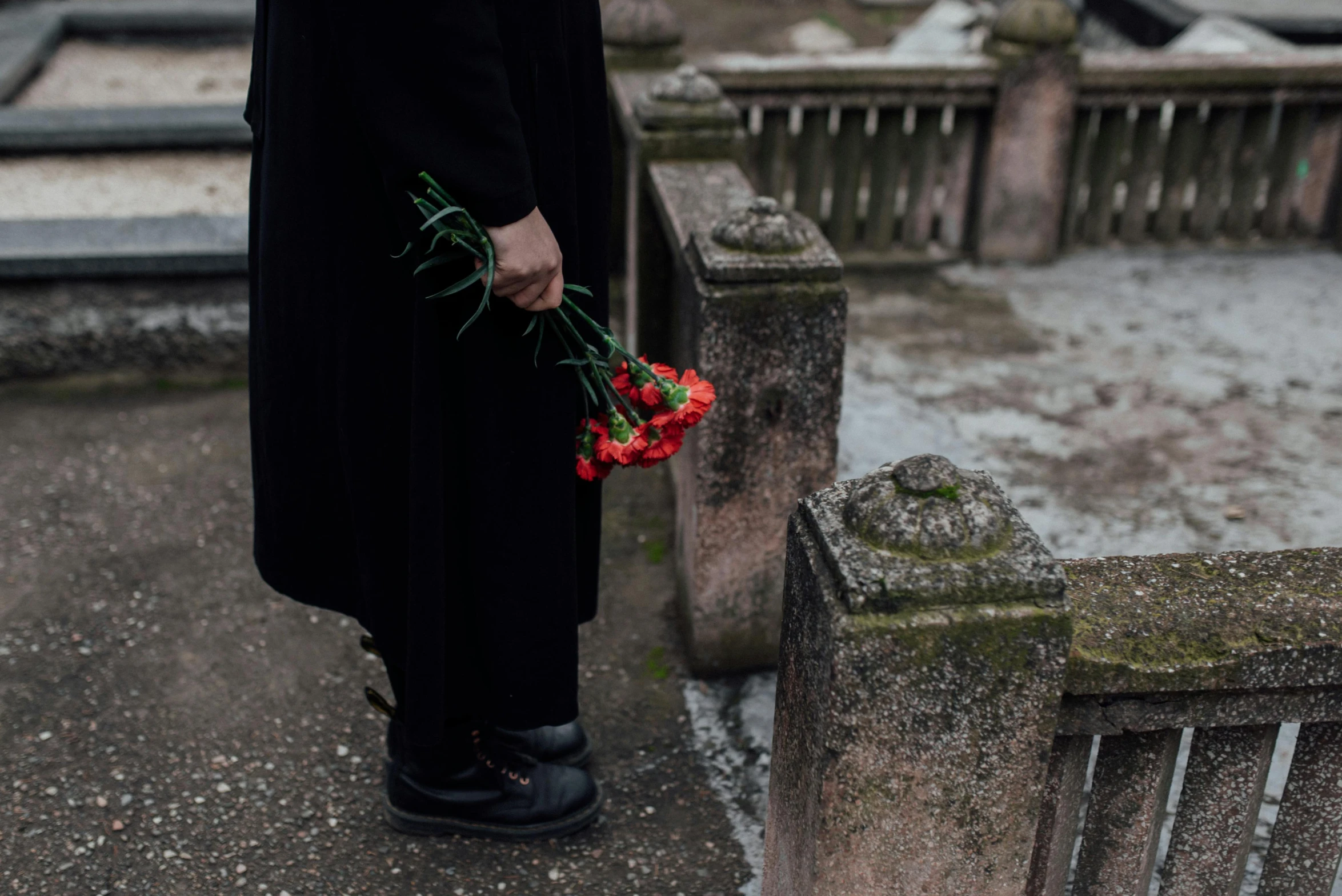 a woman is standing next to a stone fence holding some flowers