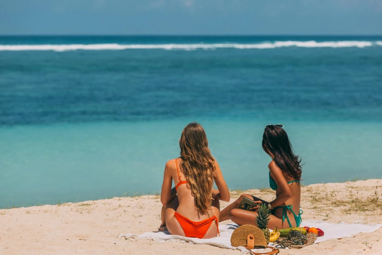 two young ladies sitting on the beach enjoying the sun