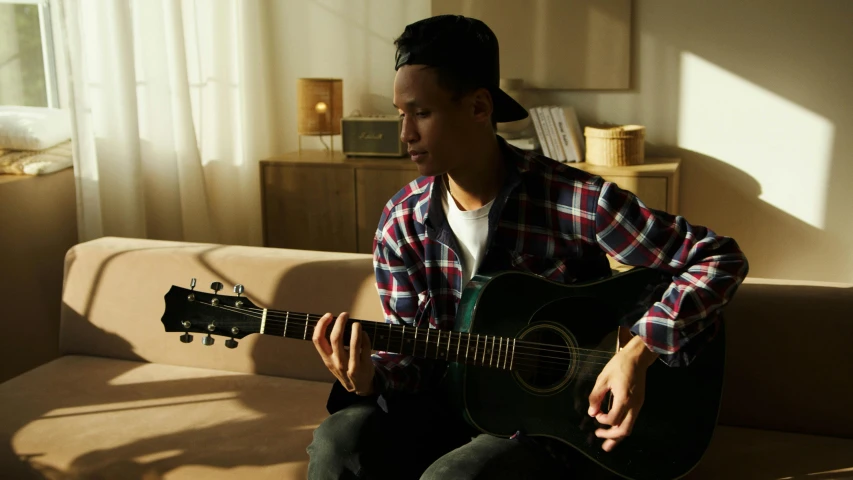 a boy sitting on a couch playing an acoustic guitar