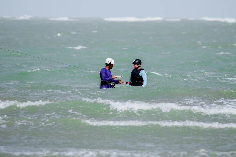 two people standing in the ocean holding onto rope