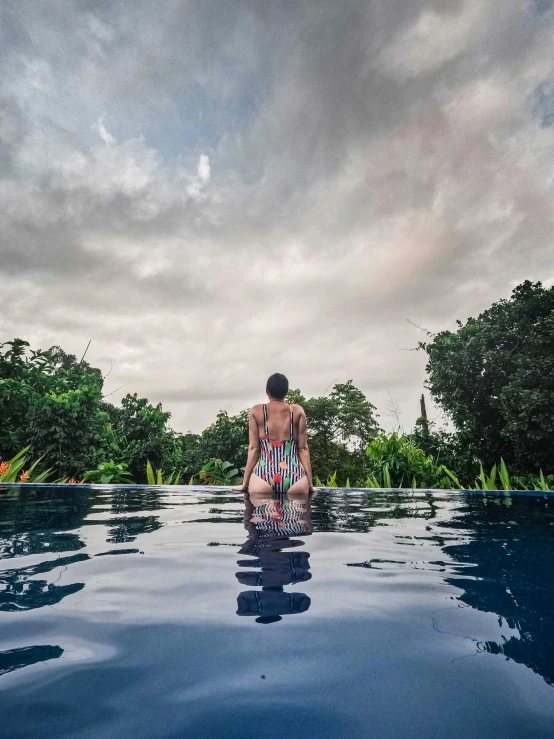 a woman sits at the end of the pool while staring into the distance