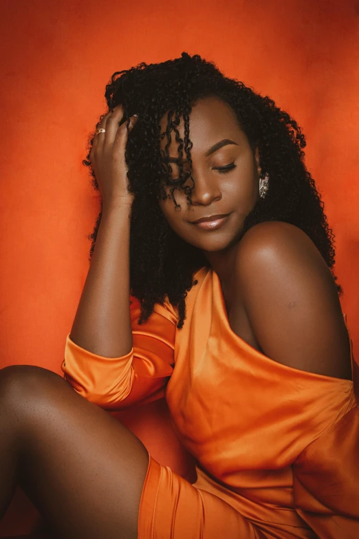 a young woman in an orange dress, sitting against an orange wall