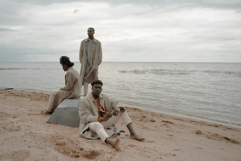 a group of three men sitting on the sand near the ocean