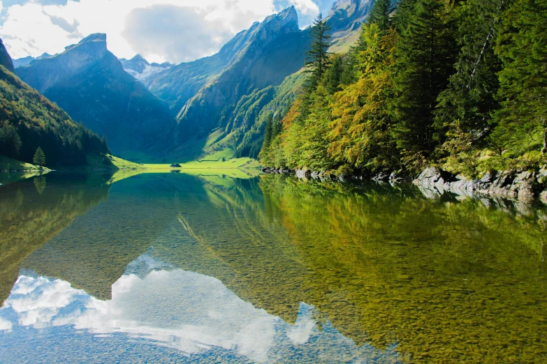 a pond surrounded by forest and mountains in a valley