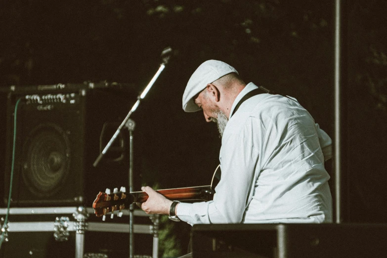 a man in white sits with a guitar on stage