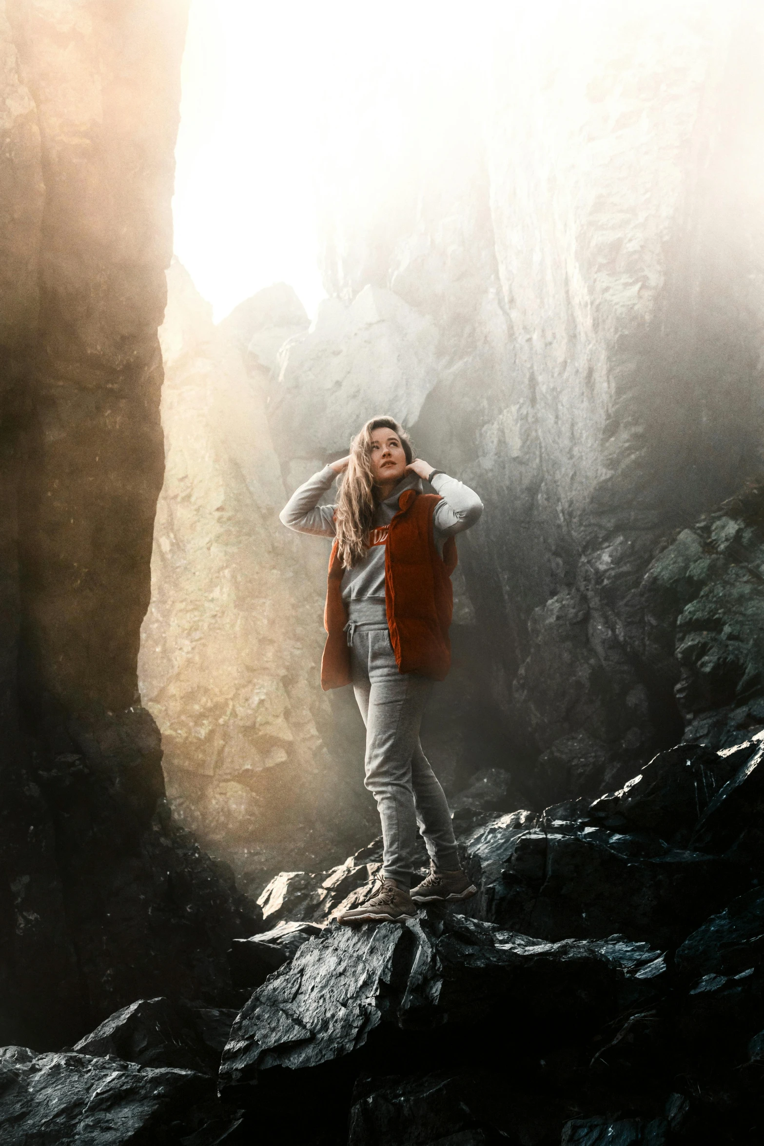 a woman in red vest standing on rocky mountain top