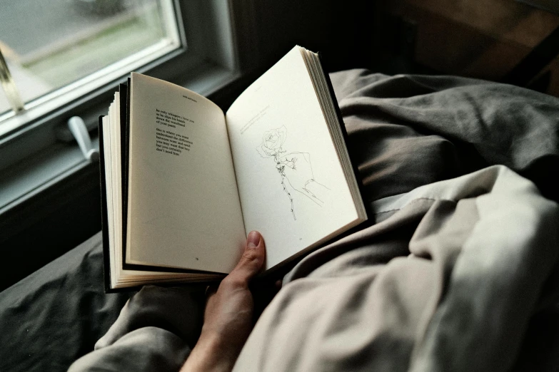 hand holding open book sitting on top of a bed