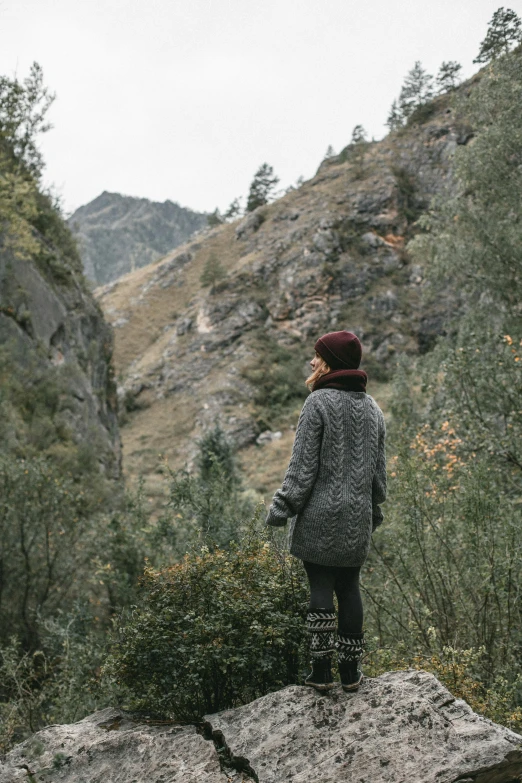 a woman standing on top of a large rock next to trees