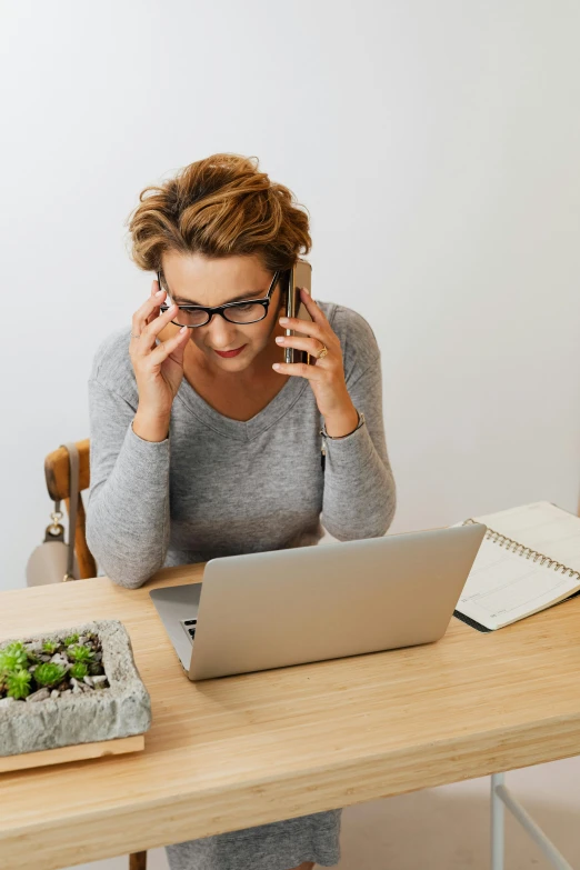 a young woman looking at a laptop computer while holding up her glasses