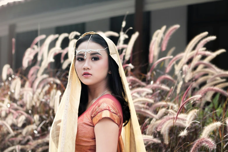 a woman wearing a yellow veil and red blouse in front of tall grass