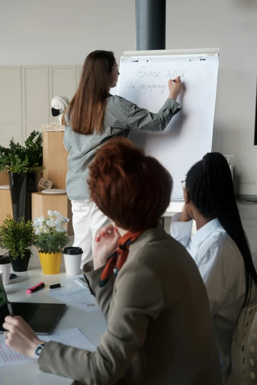 a woman stands next to a man who is writing on a dry erase board