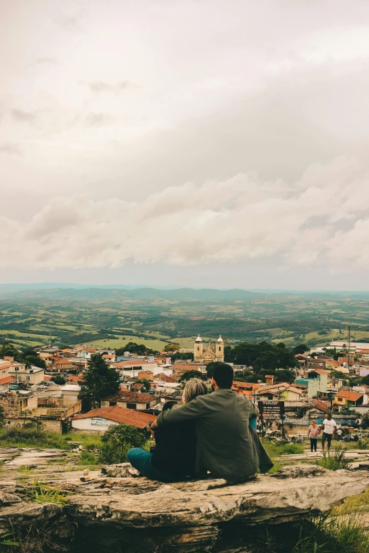 a man sits alone on top of a hill overlooking town