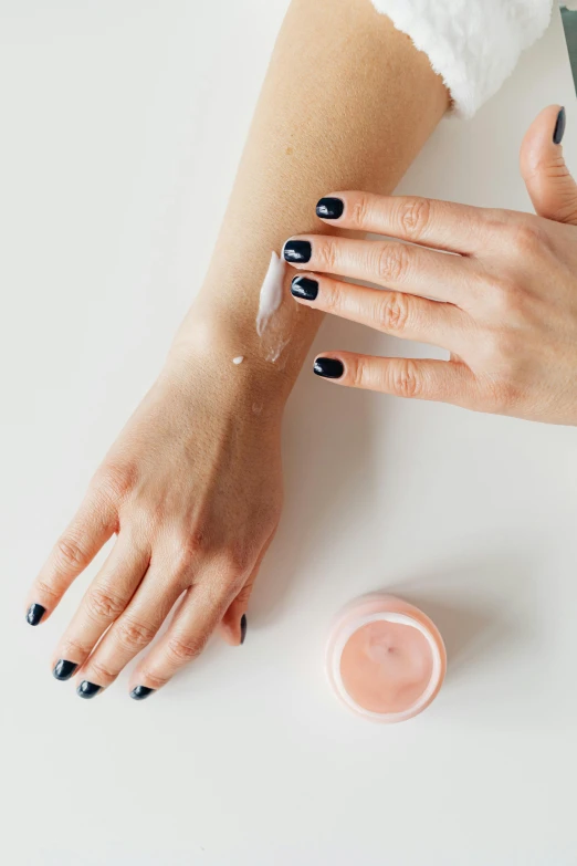 two hands on top of a counter with a round container of cream