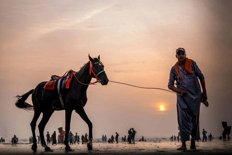 a man guiding his horse down the beach while the sun goes down