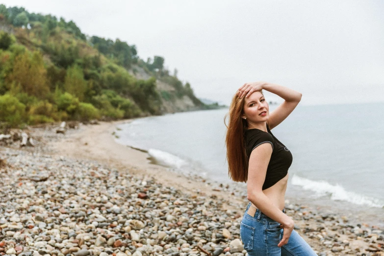 a young woman wearing a black shirt and jeans standing on the beach