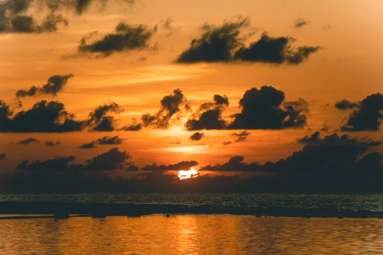 a body of water with some clouds and the sun setting