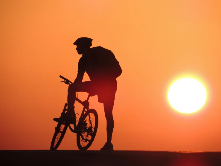 the man is standing with his bike near a sunset