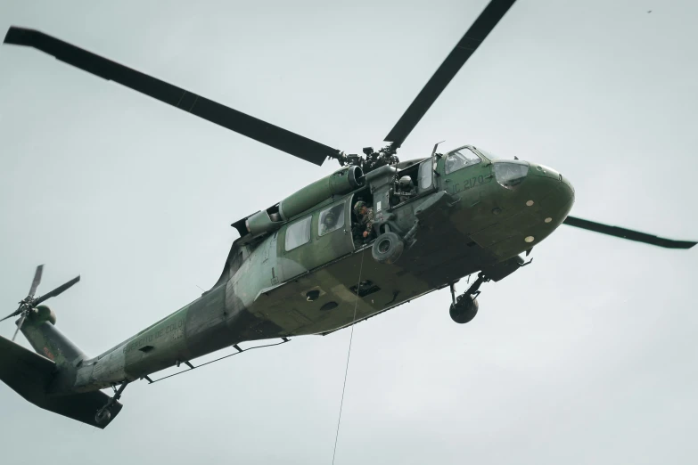 a military helicopter flies in the air with its landing gear down