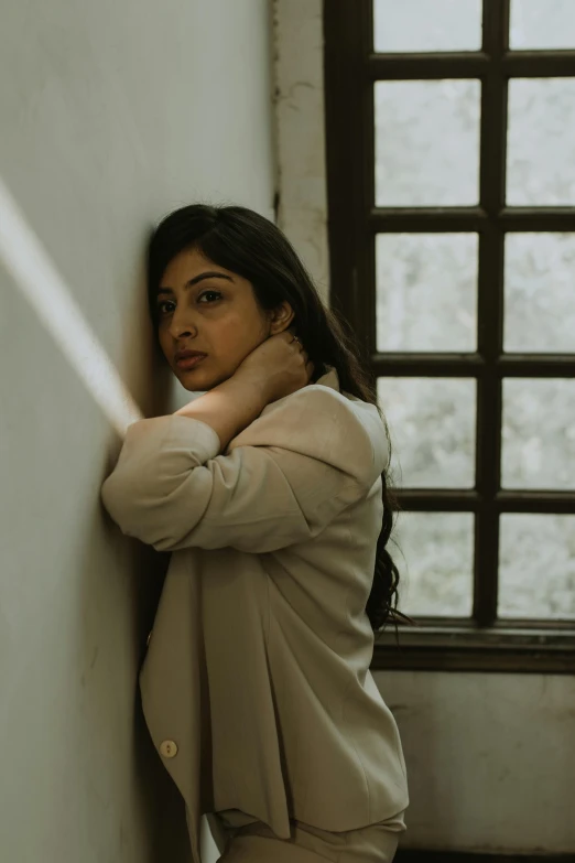 woman leaning against wall in building with window and a cigarette