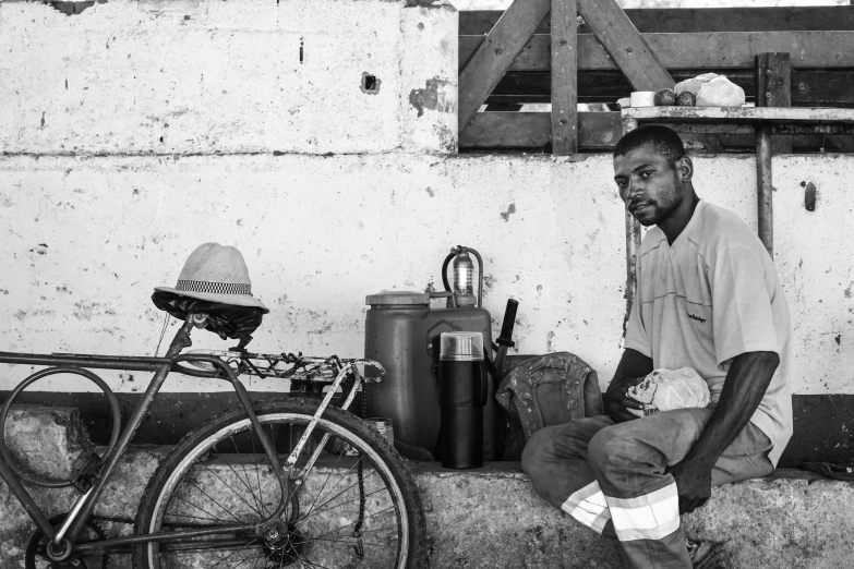 the man is sitting beside his bicycle in the dirt