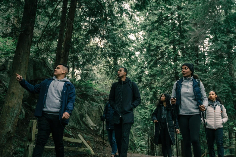 a group of young people are looking up at the sky in the woods