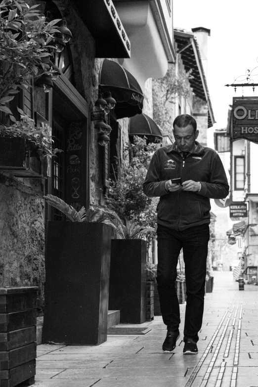 black and white pograph of man walking on a city sidewalk with an umbrella