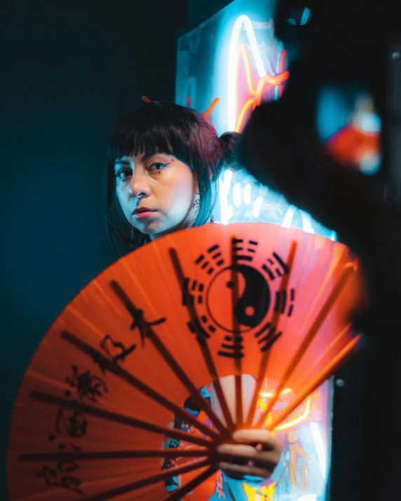 woman holding orange and black fan behind bright red light