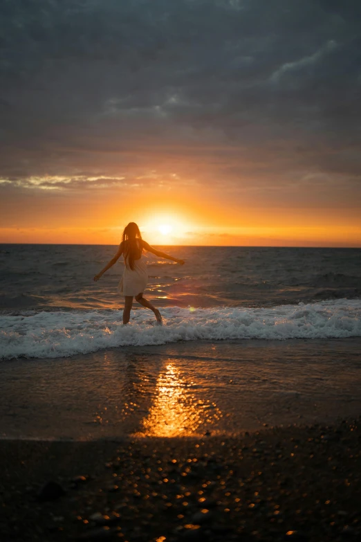 a woman is jumping on the beach at sunset