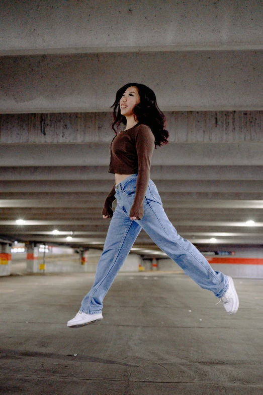 a woman wearing blue jeans and a brown shirt flying through a parking garage