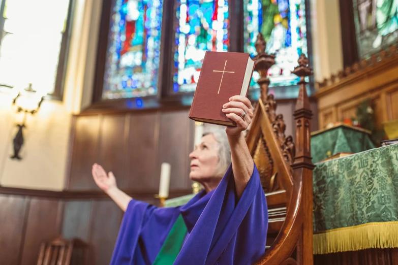 a woman holding a bible over her head in front of a window