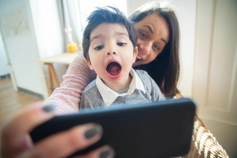 a little boy standing next to a woman while holding a tablet