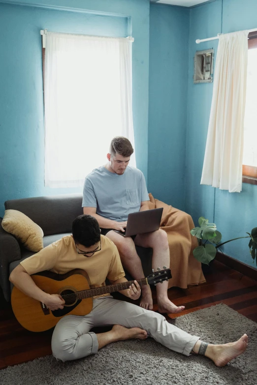 two men are sitting on the couch playing music instruments