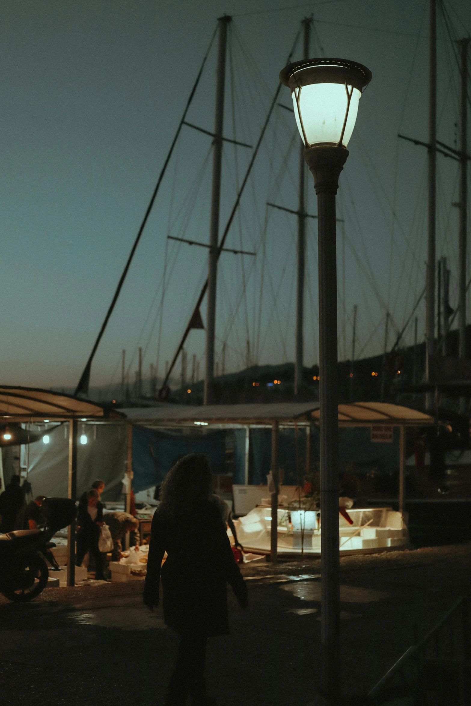 people are walking near boats under the light at night