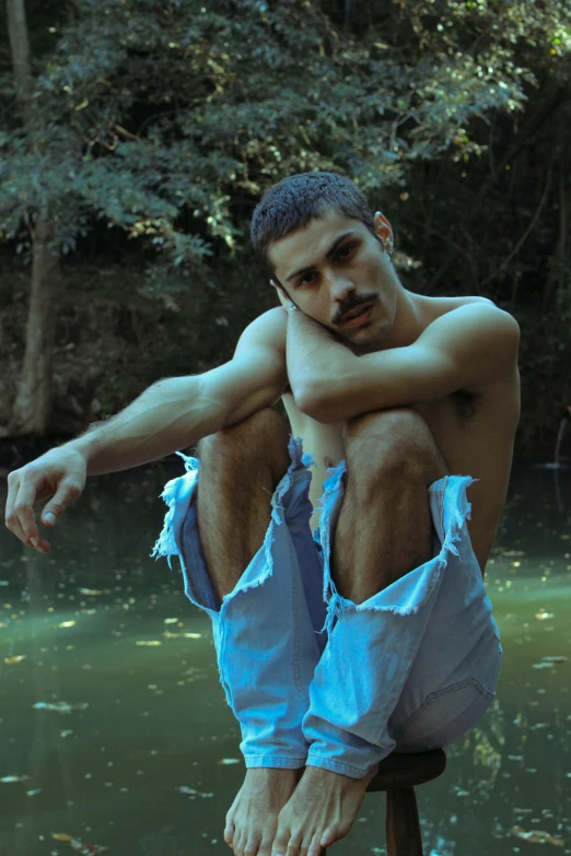 a man sitting on top of a stool near a river