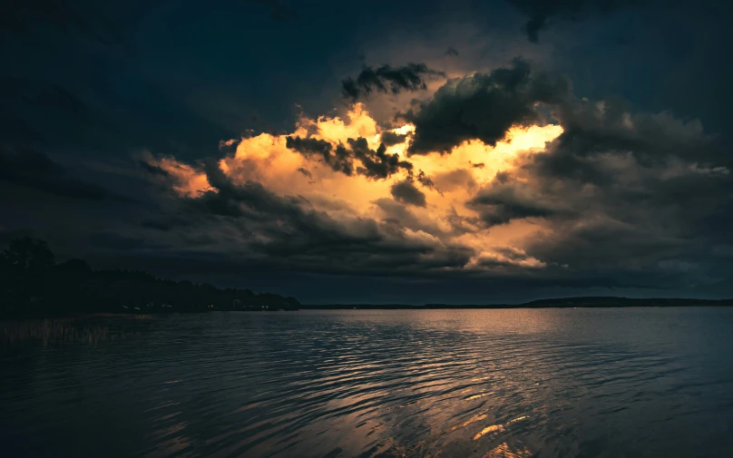 storm clouds above the water at night with light shining through